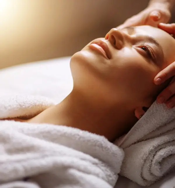 An esthetician gently touches a woman's scalp during a facial skin care service.